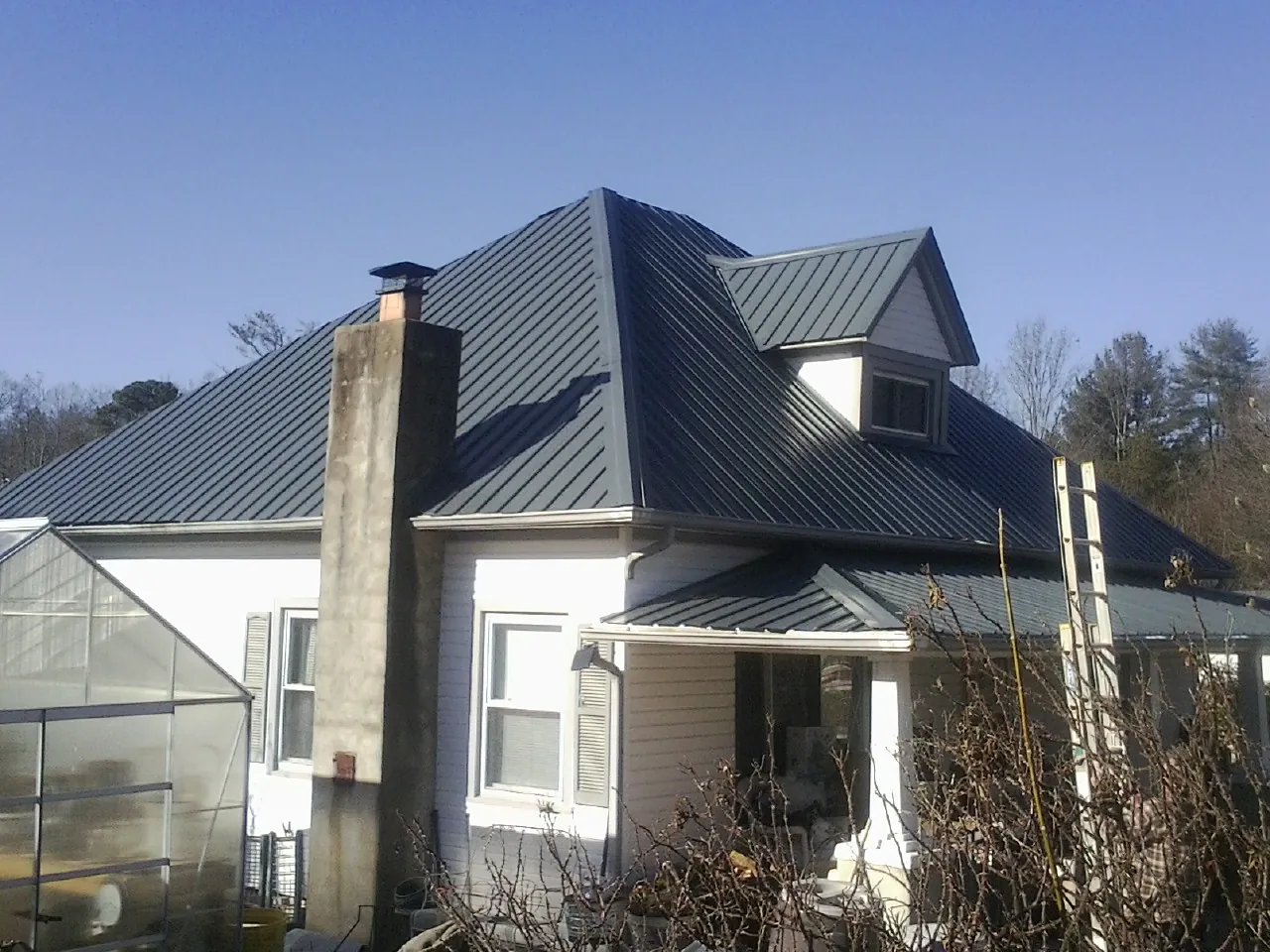 Dark blue standing seam metal roof on a white farmhouse with dormer — Slate & Tile Roof Repair by Roofing Brothers in Drake