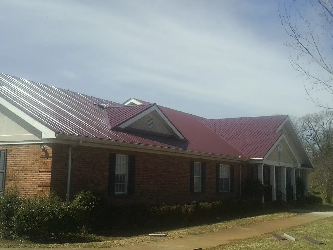 Red metal roof with gabled entries on a long brick building, from a Hail Damage Roof Repair job in Drake