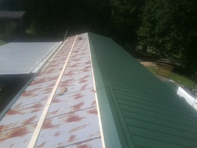 Old rusted panels beside newly installed green metal roofing — Wind Damage Roof Repair by Roofing Brothers in Drake