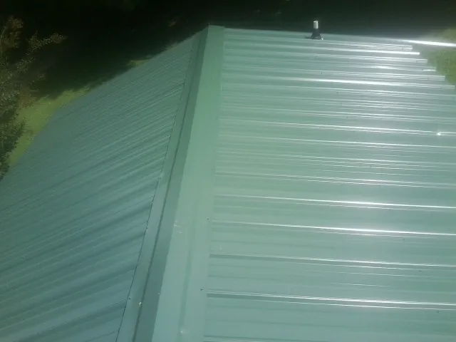 New green metal panels meeting at the ridge of a roof — Flat Roof Repair work by our crew in Drake