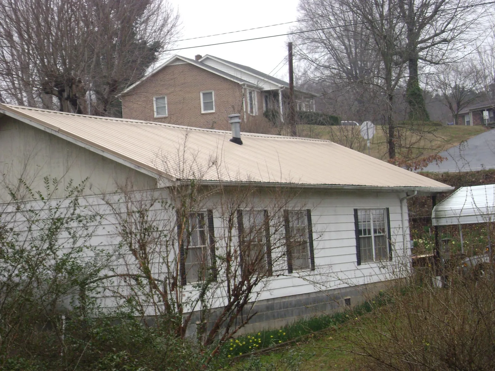 Tan metal roof on a white sided house set into a hillside — Commercial Roofing by Roofing Brothers in Drake