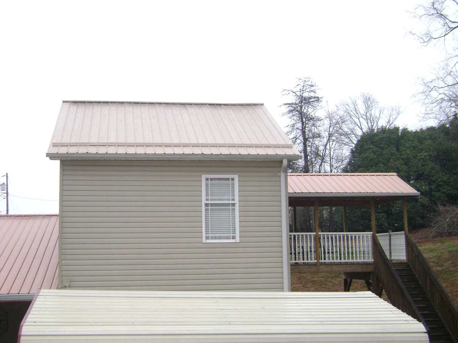 Tan metal roofs on a two story addition and attached porch, from a Roof Replacement job in Drake
